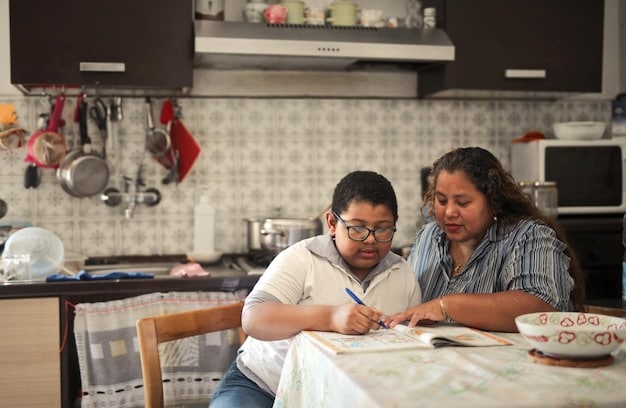 A Filipino mother is helping her son with his homework at the dining table. There are books and papers scattered around, and the mother is pointing at the book while explaining something to her son.