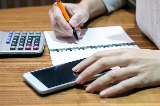 A hand writing down expenses in a notebook while using a calculator, showing budget planning and financial tracking.